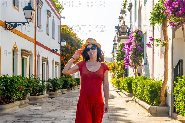 A woman walking in a red dress in the port of the flower-filled coastal town Mogan in the south of Gran Canaria. Spain