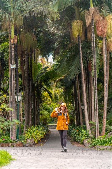 A tourist woman walking in a tropical botanical garden with large palm trees along a path, vertical photo