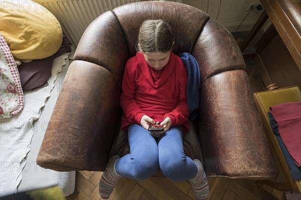 Symbol photo mobile phone, internet, addiction, little girl, 10 years old, sitting in an armchair with her mobile phone, Mecklenurg-Vorpommern, Germany, Europe