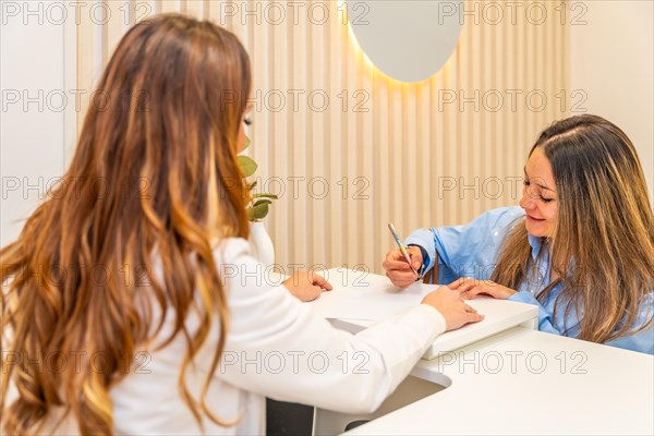 Woman filling a form in the reception of a beautician surgery clinic attended by a doctor