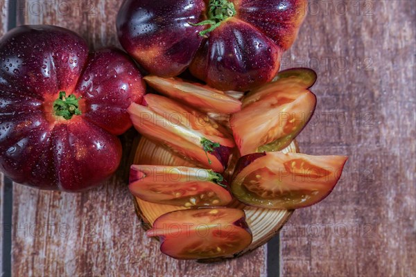 Top view of a group of tasty fresh tomatoes of the blue variety with a sliced tomato soaked with water drops on a wooden table