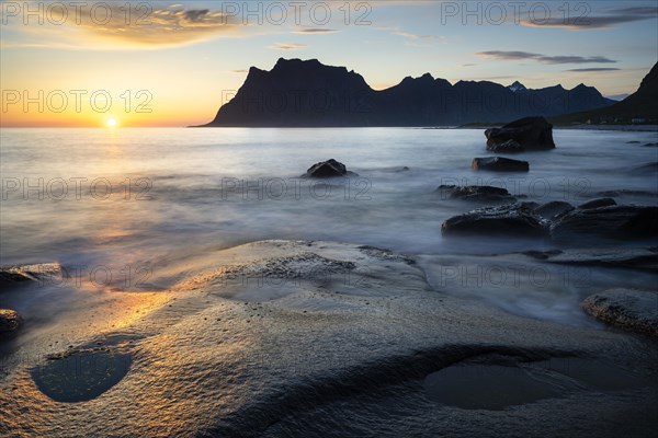 Seascape on the beach at Uttakleiv (Utakleiv), rocks in the foreground. Mount Hogskolmen in the background. At night at the time of the midnight sun. The sun is low in the sky. Early summer. Long exposure. Uttakleiv, Vestvagoya, Lofoten, Norway, Europe