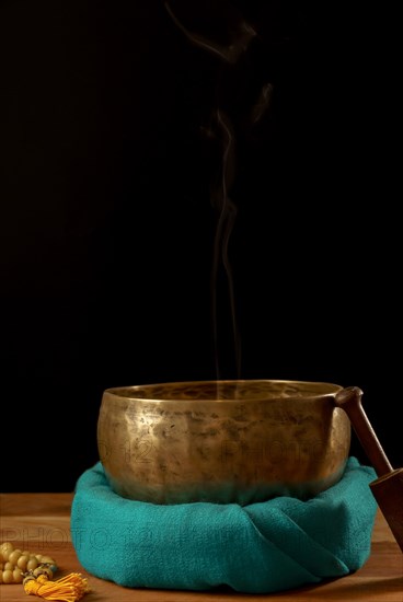 Tibetan singing bowl smoking on green cloth next to a Buddhist japa mala isolated on black background with copy space