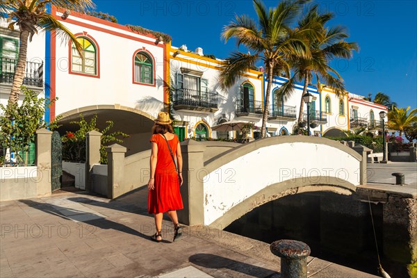 A tourist woman in a red dress walking in the port of the town Mogan in Gran Canaria in summer