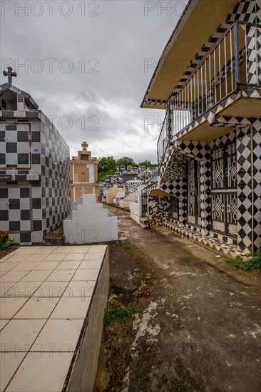 Famous cemetery, many mausoleums or large tombs decorated with tiles, often in black and white. Densely built buildings under a dramatic cloud cover Cimetiere de Morne-a-l'eau, Grand Terre, Guadeloupe, Caribbean, North America