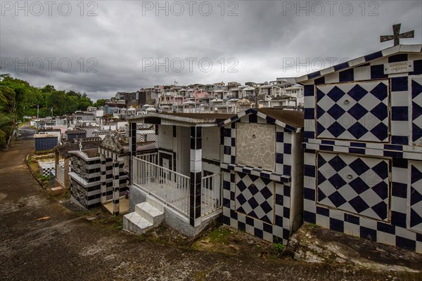 Famous cemetery, many mausoleums or large tombs decorated with tiles, often in black and white. Densely built buildings under a dramatic cloud cover Cimetiere de Morne-a-l'eau, Grand Terre, Guadeloupe, Caribbean, North America