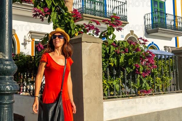 A tourist woman with a red dress in the port of the town Mogan in Gran Canaria leaving a house. Spain