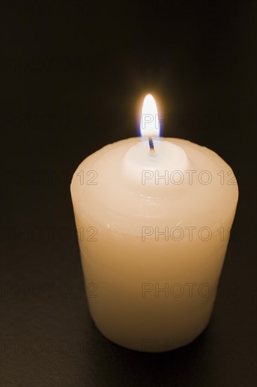 Close-up of white wax candle with bright lit flame on black background, Studio Composition, Quebec, Canada, North America