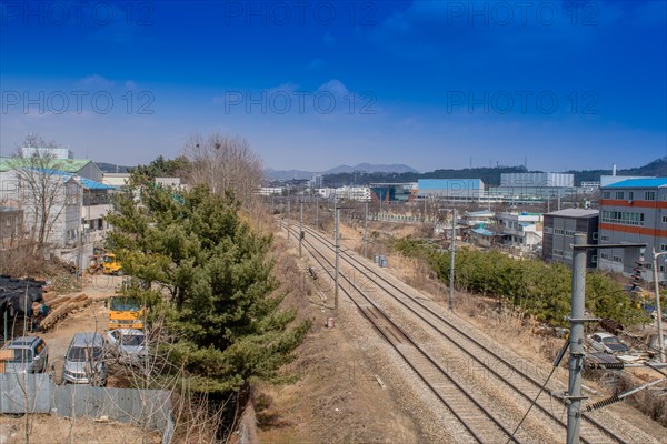 Train tracks running through industrial area on outskirts of small town framed by industrial buildings in South Korea