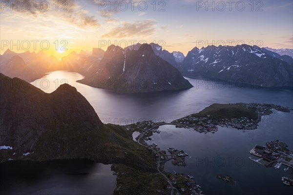 Mountain landscape, view from Reinebringen mountain to the village of Reine and Gravdalsbukta (Gravdals Bay), Olstinden mountain in the centre, Lilandstinden mountain on the right. On the left the Reinefjord with other mountains. At night at the time of the midnight sun in good weather. The sun is above the mountains. Early summer. Reine, Moskenesoya, Lofoten, Norway, Europe
