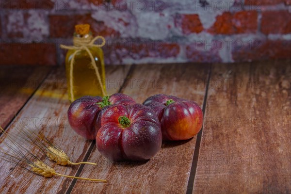 Group of tasty fresh blue tomatoes on a wooden table next to ears of wheat with a bottle of olive oil in the background