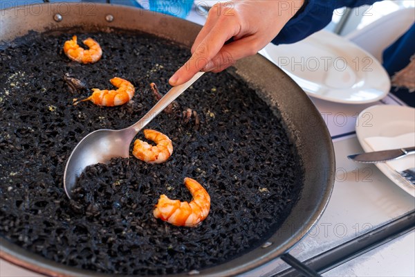 A spoon serving black rice with prawns and squid, a dry rice, cooked in paella or in a clay pot, a characteristic flavor of Valencian Mediterranean cuisine. Spain
