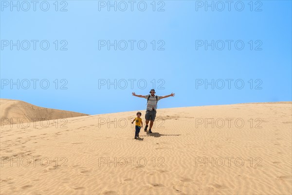 Father and son enjoying going down the dunes of Maspalomas, Gran Canaria, Canary Islands