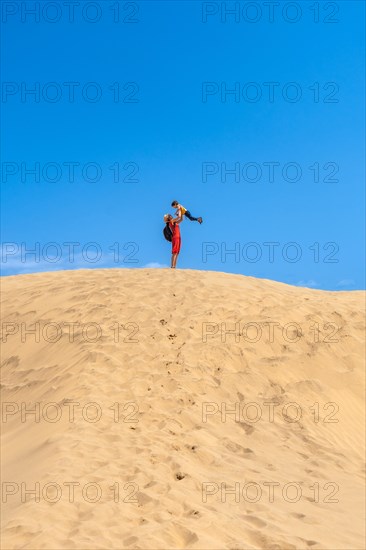 Mother lifting child smiling in the dunes of Maspalomas on vacation, Gran Canaria, Canary Islands