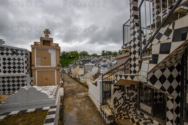 Famous cemetery, many mausoleums or large tombs decorated with tiles, often in black and white. Densely built buildings under a dramatic cloud cover Cimetiere de Morne-a-l'eau, Grand Terre, Guadeloupe, Caribbean, North America