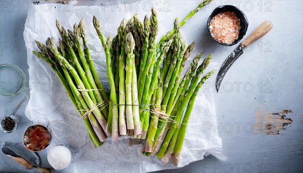 Fresh green asparagus lies bundled next to sea salt and cooking utensils on a wooden board, KI generated, AI generated