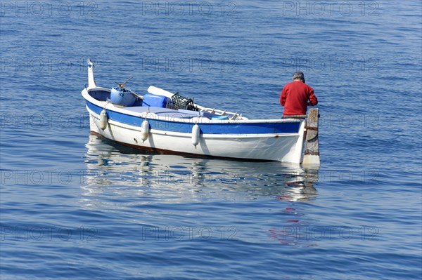 A fisherman, A calm blue sea with a small boat and a man in red, Marseille, Departement Bouches-du-Rhone, Region Provence-Alpes-Cote d'Azur, France, Europe