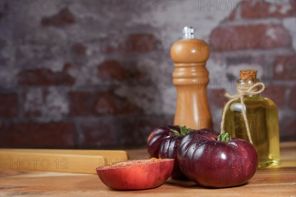 Group of tasty fresh tomatoes of the blue variety together with wooden tongs, a glass bottle of olive oil and a pepper shaker on a wooden table