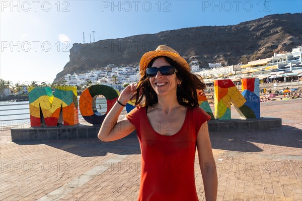 A woman in a red dress on the tourist sign in the coastal town of Mogan in the south of Gran Canaria. Spain