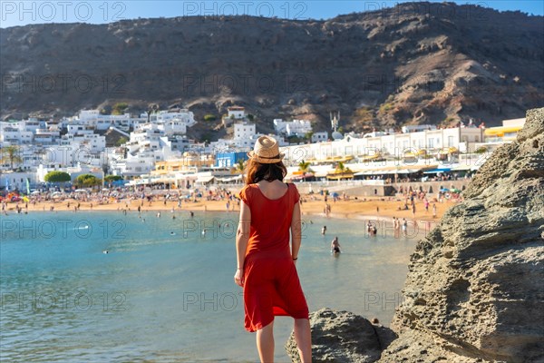 A woman in a red dress looking at the beach of the coastal town Mogan in the south of Gran Canaria. Spain