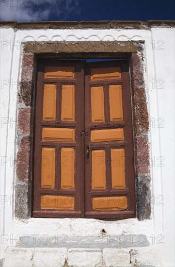 Old brown and orange painted wooden entrance doors on exterior of white roughcast cladded residential building, Fira village, Santorini, Greece, Europe