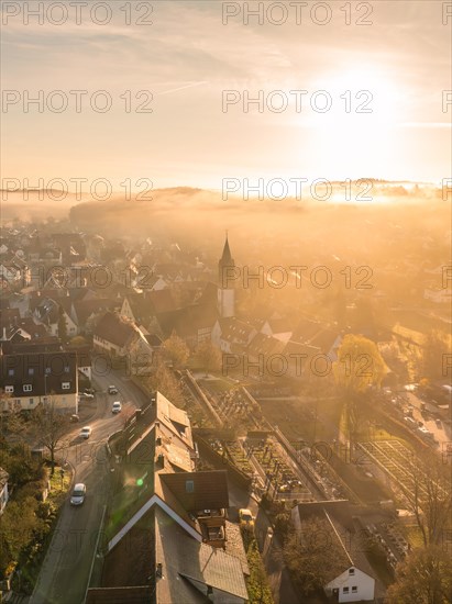 Warm morning light falls on a small town with a visible church tower through the fog, Gechingen, Black Forest, Germany, Europe