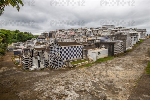 Famous cemetery, many mausoleums or large tombs decorated with tiles, often in black and white. Densely built buildings under a dramatic cloud cover Cimetiere de Morne-a-l'eau, Grand Terre, Guadeloupe, Caribbean, North America