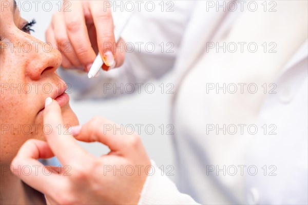 Close-up of the hands of a cosmetologist marking middle-aged woman's face for beauty treatment