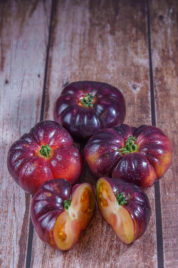 Group of tasty fresh tomatoes of the blue variety with a halved tomato dipped in water drops on a wooden table dipped in water drops on a wooden table