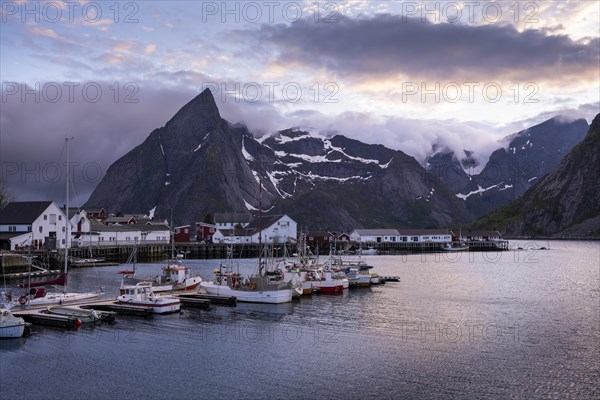 The village of Hamnoy. Houses and boats in a small harbour. Mount Olstinden in the background. At night at the time of the midnight sun in good weather, some clouds in the sky. Early summer. Hamnoy, Moskenesoya, Lofoten, Norway, Europe