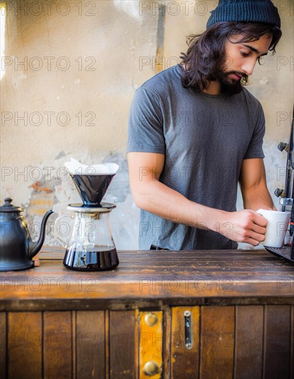 An earnest barista in a black t-shirt brews coffee on a wooden counter with a modern, minimalistic grinder, Vertical aspect ratio, AI generated