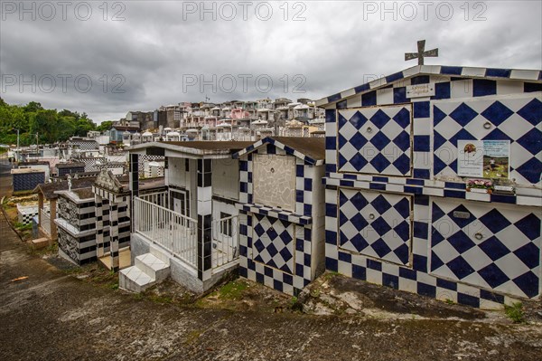 Famous cemetery, many mausoleums or large tombs decorated with tiles, often in black and white. Densely built buildings under a dramatic cloud cover Cimetiere de Morne-a-l'eau, Grand Terre, Guadeloupe, Caribbean, North America