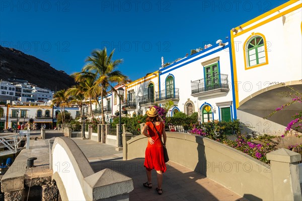 A tourist woman in a red dress on a bridge in the port of the town Mogan in Gran Canaria. Spain