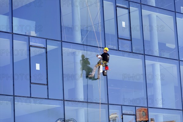 Marseille harbour, window cleaner secured by ropes to a reflective glass facade of a tall building, Marseille, Departement Bouches-du-Rhone, Provence-Alpes-Cote d'Azur region, France, Europe