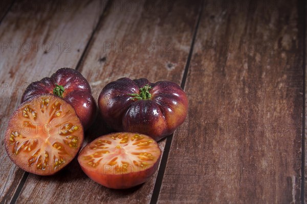 Group of tasty fresh tomatoes of the blue variety with a halved tomato dipped in water drops on a wooden table dipped in water drops on a wooden table