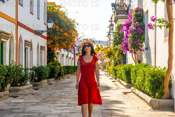 A woman walking in a red dress in the flower-filled port of Mogan town in the south of Gran Canaria. Spain