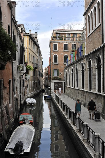 Canal in Venice with boats, surrounded by historic buildings and people walking, Venice, Veneto, Italy, Europe