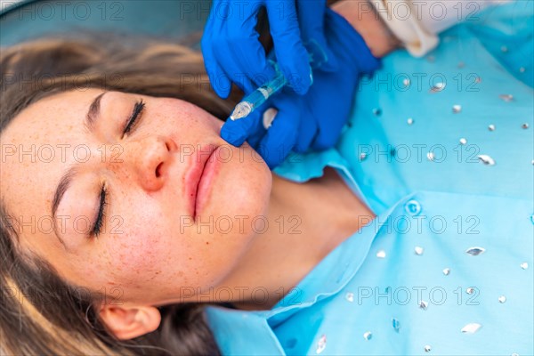 Close-up top view of a caucasian adult woman lying on stretcher with eyes closed during a beauty facial rejuvenation treatment with hyaluronic acid in a clinic