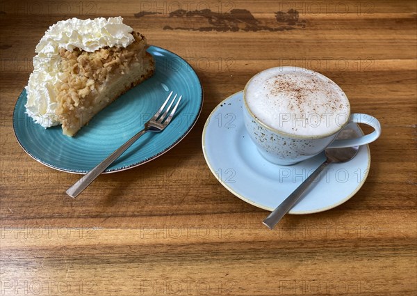 Cup of cappuccino, teaspoon and piece of apple pie with whipped cream on plate, cake fork, wooden table, Frankfurt am Main, Hesse, Germany, Europe