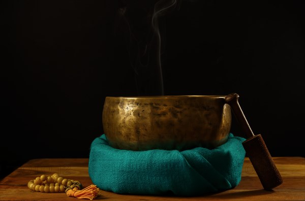 Tibetan singing bowl smoking on green cloth next to a Buddhist japa mala isolated on black background with copy space