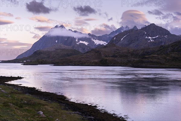 Mountain landscape on the Lofoten Islands. View from Flakstadoya across the sea to Moskenesoya. At night at the time of the midnight sun. Good weather, some lenticular clouds in the sky. Early summer. Lofoten, Norway, Europe