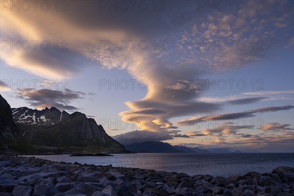 Cloudscape, view from Hamnoy over the sea along Moskenesoya, Flakstadoya and Vestvagoya. Several coloured lenticular clouds (lenticularis) in the blue sky. At night at the time of the midnight sun in good weather. Early summer. Lofoten, Norway, Europe