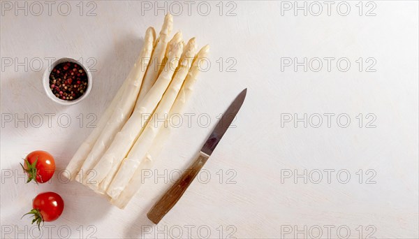 Fresh white asparagus next to tomatoes, a pepper mill and a knife on a light-coloured surface, AI generated, AI generated