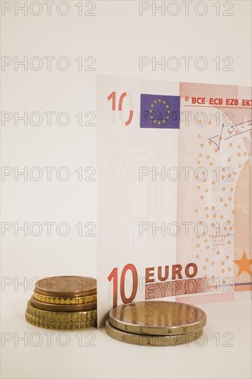 Close-up of 10 Euro bank note and piles of assorted gold and copper colored coins on white background, Studio Composition, Quebec, Canada, North America