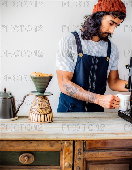 A tattooed barista manually brews coffee, demonstrating individuality and a vintage vibe, Vertical aspect ratio, AI generated