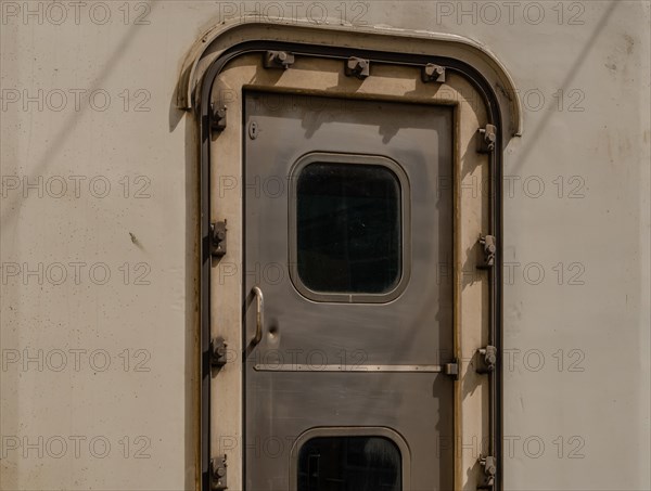 Close-up of a metallic train door with a small window and rivets, in South Korea