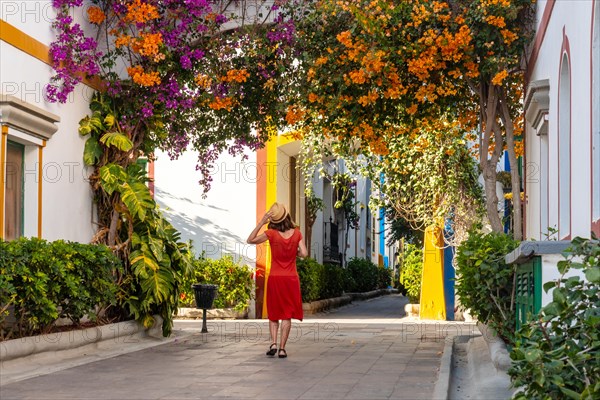 A tourist woman with a red dress in the port of the Mogan town full of flowers in the south of Gran Canaria. Spain