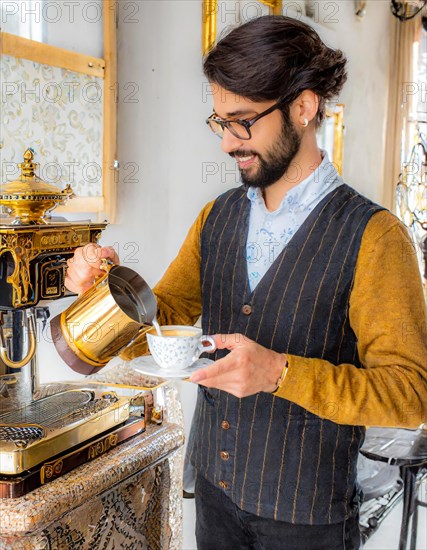 An elegant man in a vest pours coffee from a golden pot in a luxurious, traditionally adorned room, Vertical aspect ratio, AI generated
