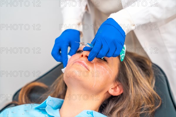 Doctor cleaning the injection area with a cotton pad on the patient's face before administering hyaluronic acid