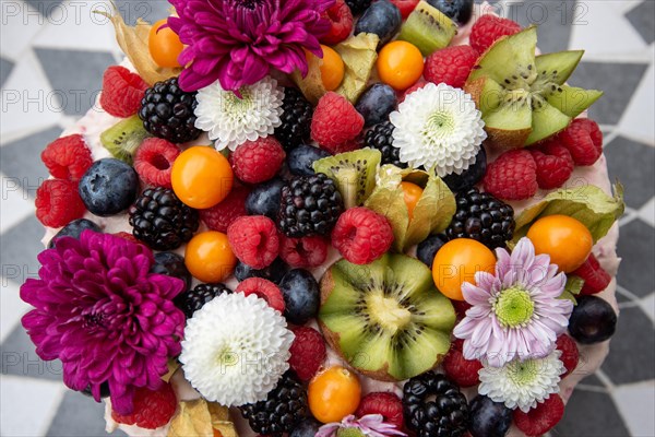 Delicious-looking cake garnished with a variety of berries and colourful flowers on a patterned base, Germany, Europe